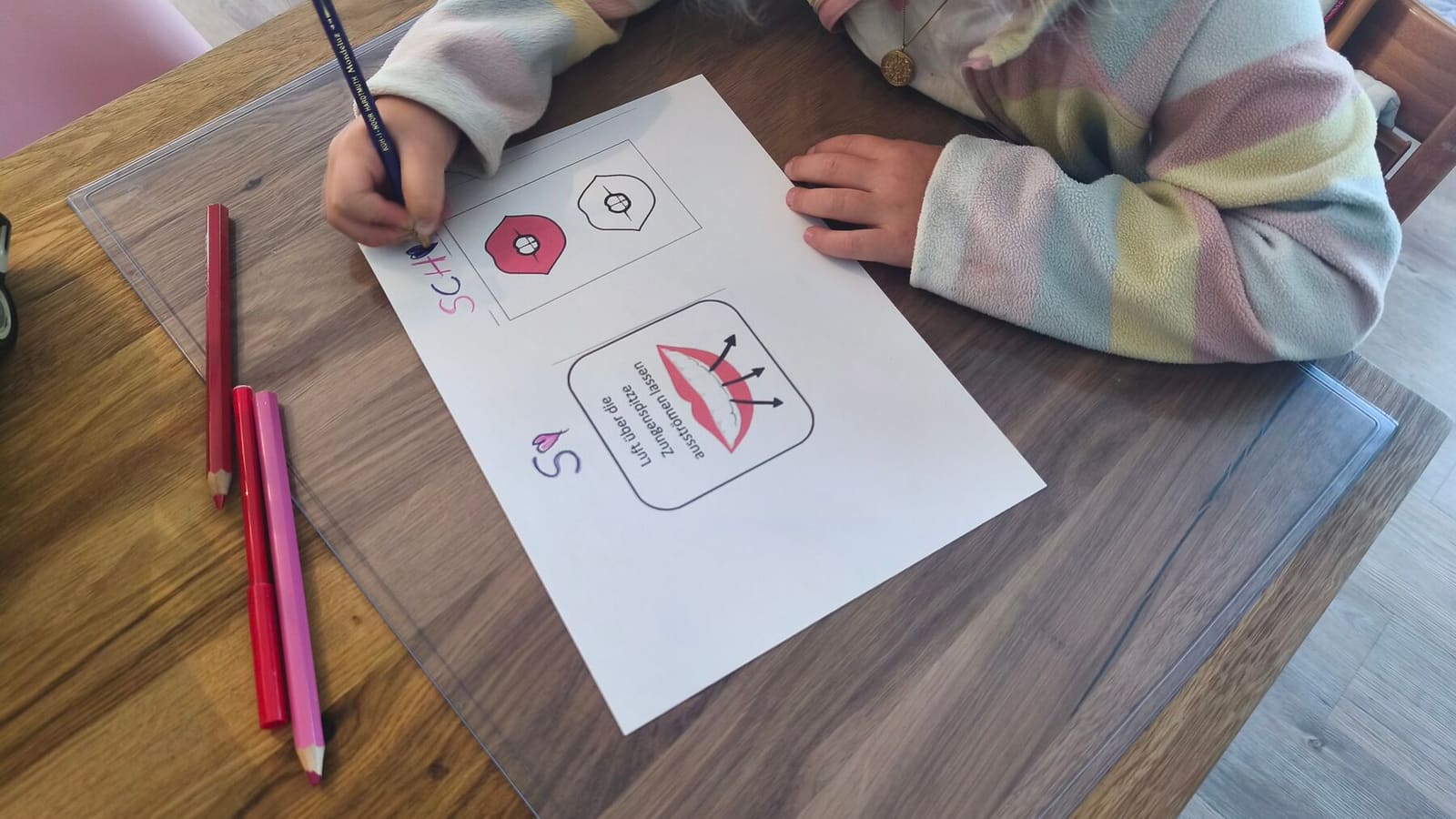 Ein Kind bearbeitet ein Arbeitsblatt zum Laut „Sch“, daneben liegen Buntstifte